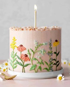 a pink cake with flowers on it and a single candle sticking out of the top