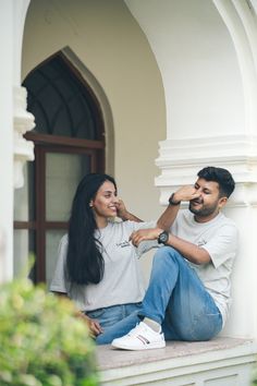 a man and woman sitting on the ledge of a building, smiling at each other