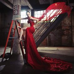 a woman in a red dress is sitting on a stair case and posing for the camera