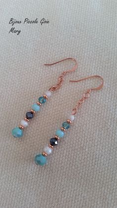 two pairs of blue and white beads are hanging from copper earwires on a beige surface