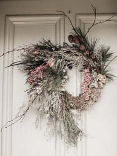 a wreath is hanging on the front door with pine cones and pink flowers in it