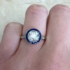 a person's hand holding a ring with a blue and white diamond in it