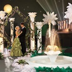 a man and woman in formal dress standing next to a fountain with lights on it