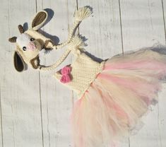 a stuffed cow wearing a pink and white tutu skirt on top of a wooden floor