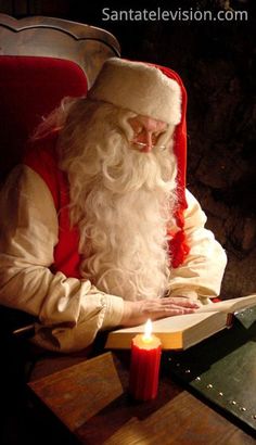 a man dressed as santa claus sitting at a table with a lit candle in front of him