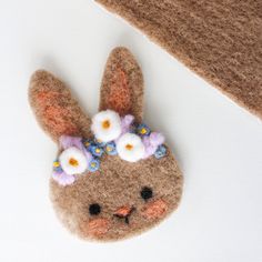 a small felt bunny with flowers on its head is laying next to a piece of fabric