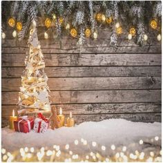 a small christmas tree sitting in the snow next to some candles and presents with lights on them