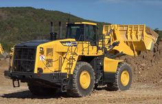 a large yellow dump truck parked on top of a dirt field next to a hill