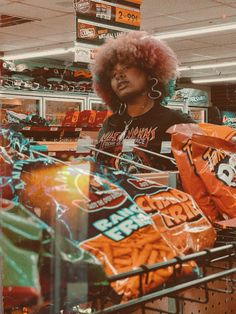 a woman with afro hair standing in a grocery store aisle next to bags of food