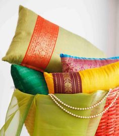 colorful pillows are stacked on top of each other in different colors and patterns, along with a beaded necklace