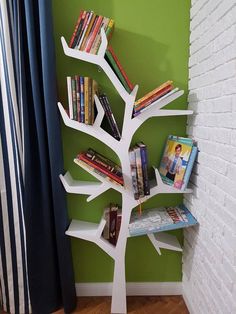 a white tree shaped book shelf with books on it in front of a green wall