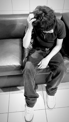 a man sitting on top of a black couch next to a white tiled floor with his head in his hands