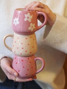 a woman holding three coffee mugs in her hands with hearts and flowers on them