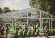 several people standing in front of a green house with plants growing out of the ground