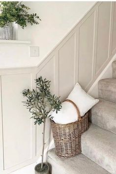 a basket sitting on the stairs next to a plant and some white pillows in front of it