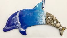 a blue and white dolphin ornament hanging from a hook with sea shells on it