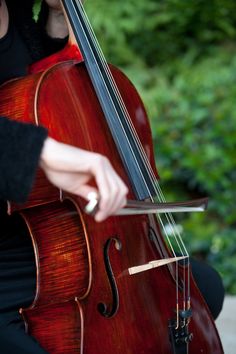 a woman is playing the cello outdoors in her black outfit and holding it with both hands