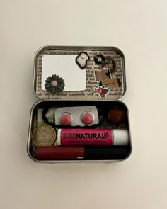 an open tin with various items in it on a table next to a white wall