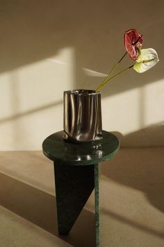 a small vase with a flower in it sitting on a table next to a wall