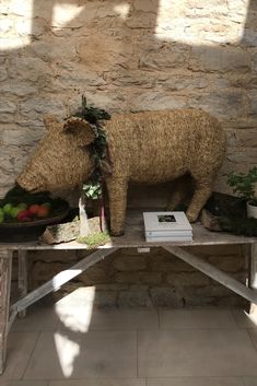 an animal made out of straw sitting on top of a table next to fruit and vegetables