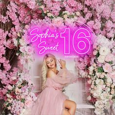 a woman in a pink dress sitting on a white bench surrounded by flowers and greenery