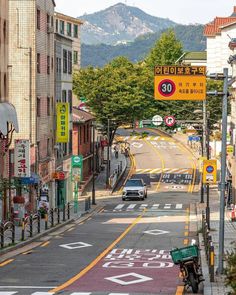 a car driving down a street next to tall buildings with mountains in the back ground