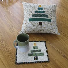 a coffee mug sits on the floor next to a pillow with a tree design and a quilted placemat