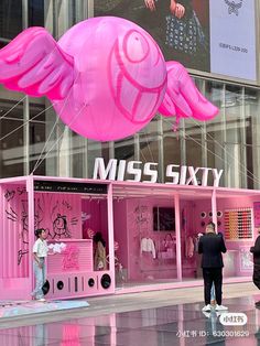 people are standing in front of a pink store with large kites attached to it