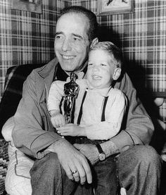 a man holding a small boy in his lap while sitting on a couch with plaid walls behind him