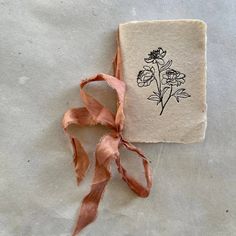 an old book with a ribbon tied around it and flowers on the front cover, sitting on top of a piece of paper