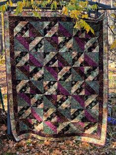 a quilt hanging from a tree branch in the fall with leaves around it and on top