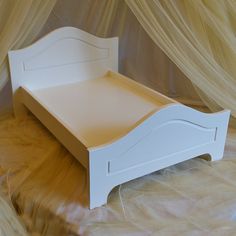 a white wooden bed frame sitting on top of a sheet covered floor next to a curtain