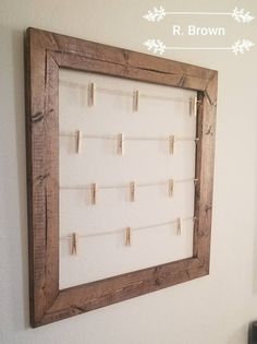 a wooden frame hanging on the wall with clothes pins attached to it and a white background