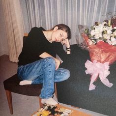 a woman sitting on a couch next to a bouquet of flowers and a book in front of her