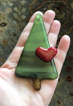 a hand holding a glass christmas tree ornament with a red heart on it