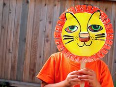 a young boy holding a paper plate with a lion face on it's head