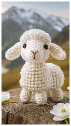 a small crocheted sheep sitting on top of a wooden table next to flowers