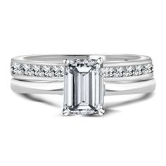 an emerald cut engagement ring with channel set diamonds on the band and side stones in white gold