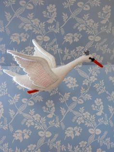 a white bird with red feet hanging from a string on a blue floral wallpaper