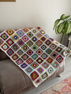 a crocheted granny blanket sitting on top of a couch next to a potted plant