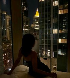 a woman sitting on top of a bed in front of a window with city lights