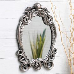 an ornate silver mirror sitting on top of a white wall next to a plant and vase