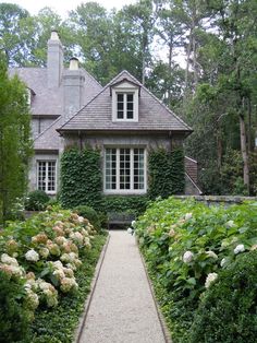 the house is surrounded by greenery and white hydrangeas in front of it