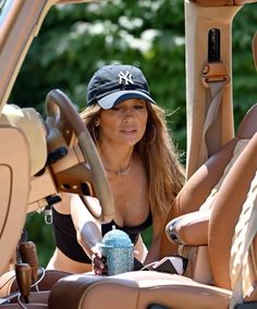 a woman sitting in the driver's seat of a car wearing a new york yankees hat