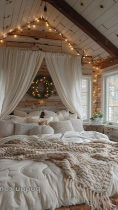 a large bed sitting under a window covered in white sheets and blankets with fairy lights hanging from the ceiling