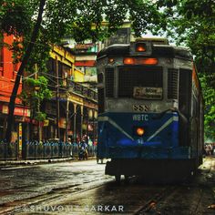 a blue and white bus driving down a street next to tall buildings in the rain