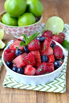 a bowl filled with fruit sitting on top of a wooden table next to limes