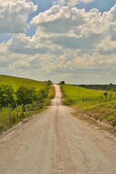 an empty dirt road in the middle of a green field