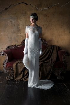 a woman standing in front of a couch wearing a white dress