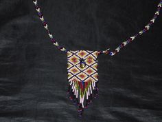 the beaded necklace is hanging on a black cloth with white beads and multicolored beads